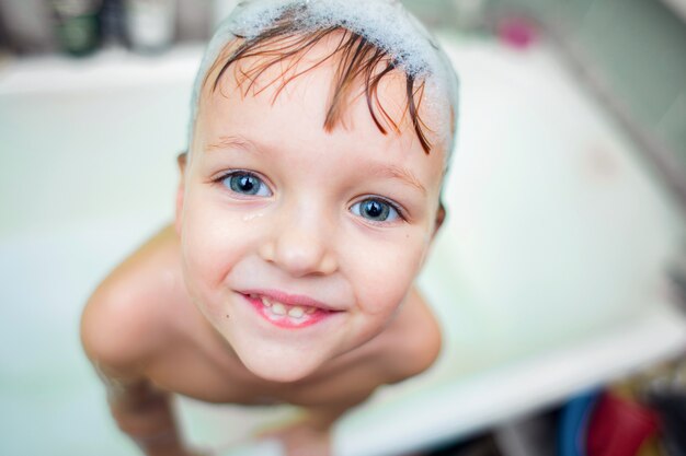 Duży portret dziecka kąpiącego się w łazience z pianką na głowie.
