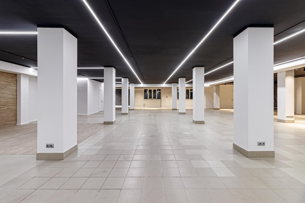 Duży pusty pokój z płytkami ceramicznymi na podłodze, czarnym sufitem z oświetleniem i kolumnami propagującymi sufit