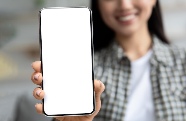 Duży pusty smartfon z białym ekranem w młodej azjatyckiej kobiecej dłoni