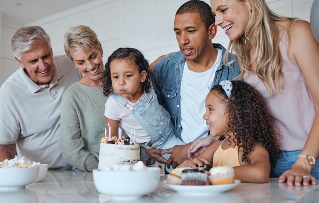 Duży rodzinny tort urodzinowy i dmuchanie świec na życzenie w domu z rodzicami, dziadkami i dziećmi razem na uroczystość Mężczyźni, kobiety i dzieci w brytyjskim domu, aby świętować na przyjęciu dla dziewczynki