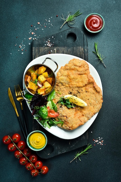 Duży smażony kurczak z warzywami na talerzu na czarnym kamiennym tle Zdjęcie jedzenia