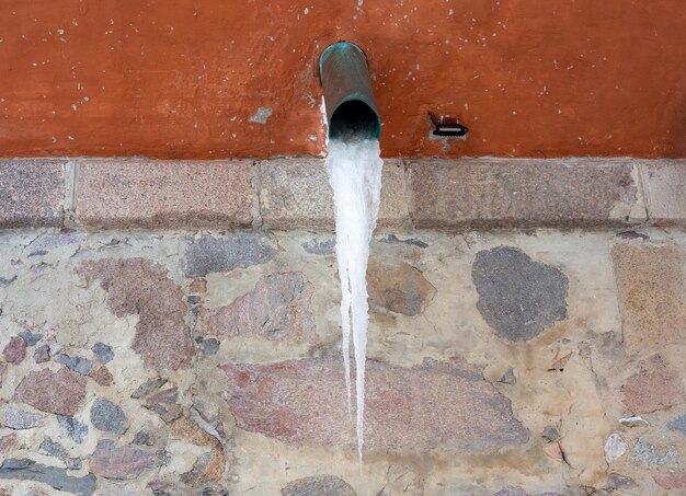 Duży sopel lodu z rynny na ścianie domu
