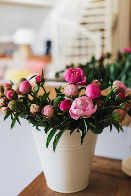Duży świeży różowo-biały bukiet kwitnących piwonii w białym metalowym wiadrze na drewnianym stole w jasnym jasnym nowoczesnym pięknym mieszkaniu Wiosenny wystrój domu lub pomysł na prezent Żywe letnie kolory