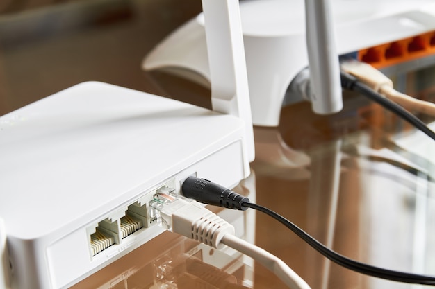 Dwa białe routery bezprzewodowe na szklanym stole połączone kablami z Internetem