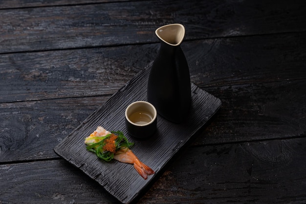 Dwa czarne wazony z małym kawałkiem sushi na drewnianej tacy.