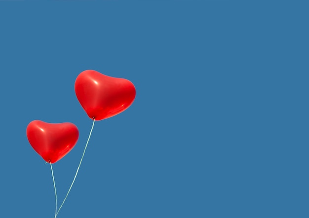 Dwa czerwone balony wypełnione helem latają po błękitnym niebie na Walentynki