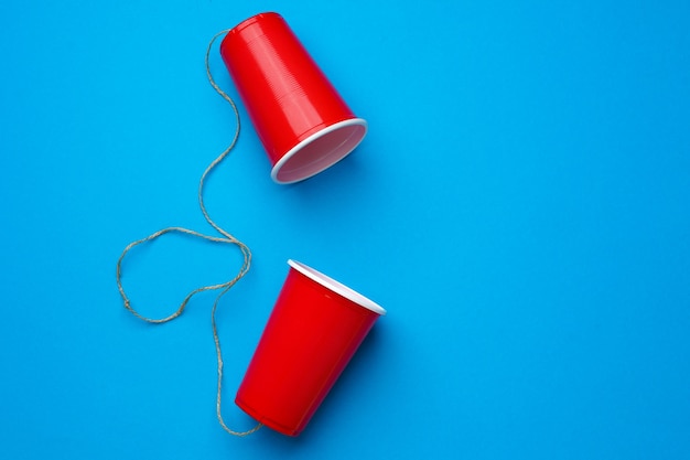 Dwa czerwone papierowe kubki połączone liną na niebieskim zabawkowym telefonie