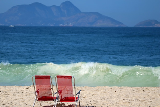 Dwa czerwoni plażowi krzesła na Copacabana plaży przeciw rozbijać ocean fala, Rio De Janeiro