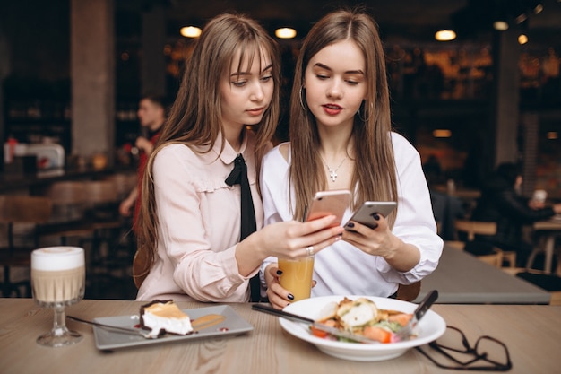 Dwa dziewczyny ma lunch w kawiarni z telefonem