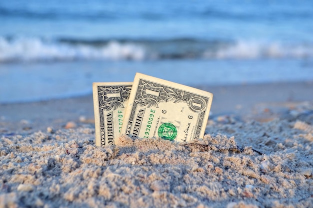 Dwa jednodolarowe banknoty do połowy zakopane w piasku na piaszczystym wybrzeżu z bliska