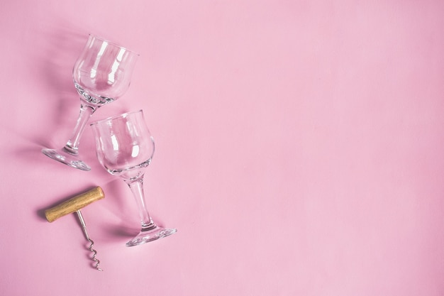 Dwa kieliszki do wina i korkociąg na różowym tle.