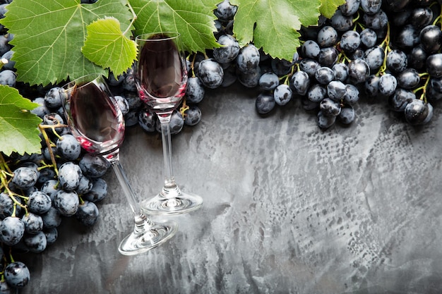 Dwa kieliszki do wina wypełnione winem leżące w ramce z winogron. Czarne soczyste winogrona Czerwone wino na ciemnym tle betonu. Skopiuj miejsce na czarnym tle porysowany. Granica.