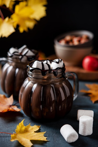 Dwa kubki aromatycznej gorącej czekolady z piankami na ciemnym tle z jesiennymi liśćmi klonu Koncepcja przytulny napój Widok z przodu i zbliżenie