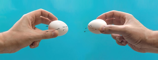 Dwa kurze jaja z grymasem lecą do siebie w rękach osoby. Wielkanoc