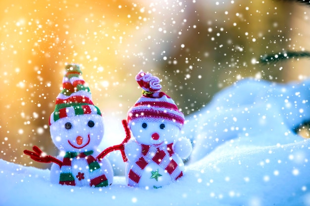 Zdjęcie dwa małe śmieszne zabawki bałwan dziecko w dzianych czapkach i szalikach w głębokim śniegu na zewnątrz na jasnym niebieskim i białym tle przestrzeni kopii. kartkę z życzeniami szczęśliwego nowego roku i wesołych świąt.