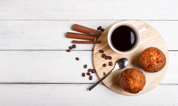 Dwa marchwianego muffins z filiżanką kawy na drewnianej kuchni wsiadają na białym drewnianym tle