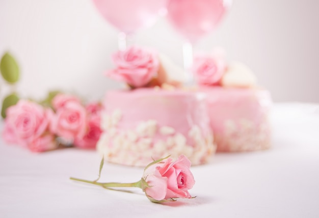 Dwa mini ciasta, szklanki z różowym winem winogronowym i kwiatami róży na białym stole. Koncepcja romantycznej kolacji. Skoncentruj się na małej róży.