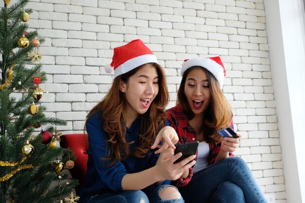 Dwa młodej ślicznej Azja kobiety trzyma smartphone i kredytową kartę podczas gdy robiący zakupy online