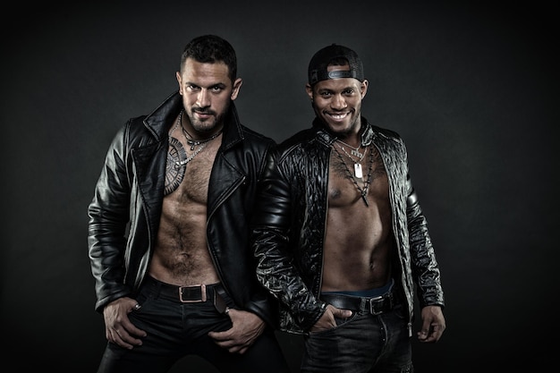 Dwa modele z wytatuowanymi skrzyniami Rowerzyści w skórzanych kurtkach Zespół rockowy na białym tle na czarnym tle Afrykańscy i kaukascy mężczyźni z seksownymi ciałami Brutalni mężczyźni noszący stylowe akcesoria moda koncepcja