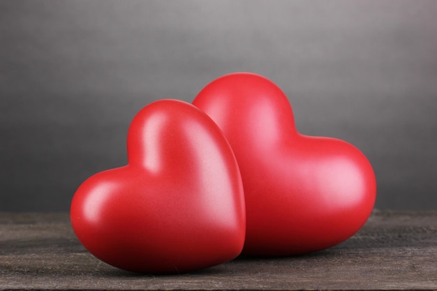 Dwa ozdobne czerwone serca na drewnianym stole na szarym tle