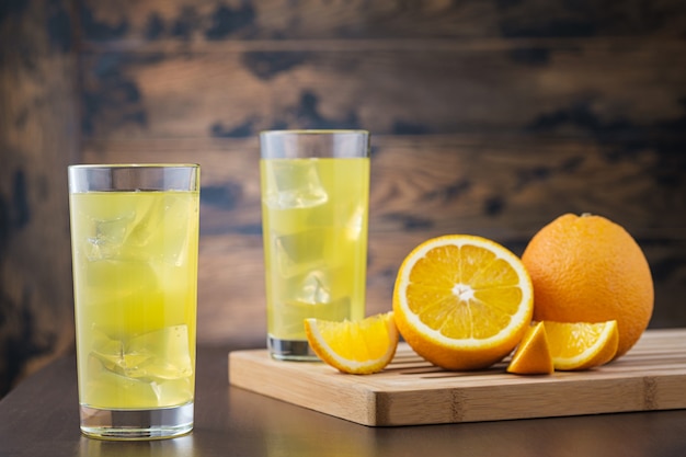 Dwa pełny sok pomarańczowy w szkle z kostkami lodu na drewnianej ścianie
