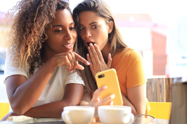 Dwa piękne młoda kobieta siedzi w kawiarni picia kawy i patrząc na telefon komórkowy.