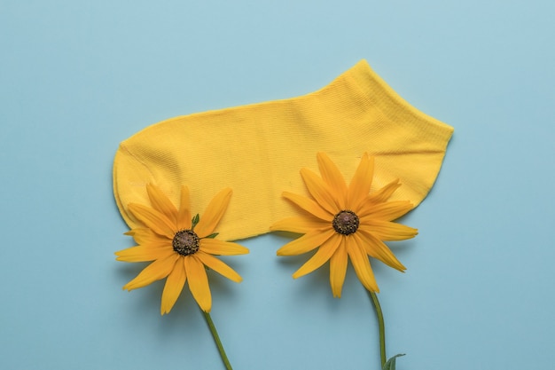 Dwa piękne żółte kwiaty i krótka sportowa skarpeta na niebieskim tle. Pojęcie wakacji letnich.