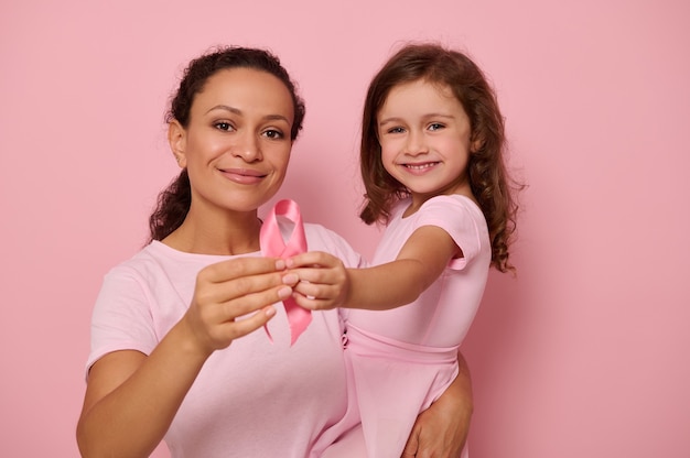 Dwa pokolenia kobiet, mama i córka przytulające się do siebie, trzymające różową wstążkę, symbol Dnia Świadomości Raka Piersi, okazujące wsparcie i solidarność pacjentom i osobom, które przeżyły raka. Zdrowie kobiet
