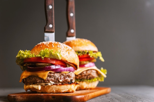 Dwa przepyszne, pyszne domowe burgery do siekania wołowiny. na drewnianym stole. Hamburgery są wstawiane noże.