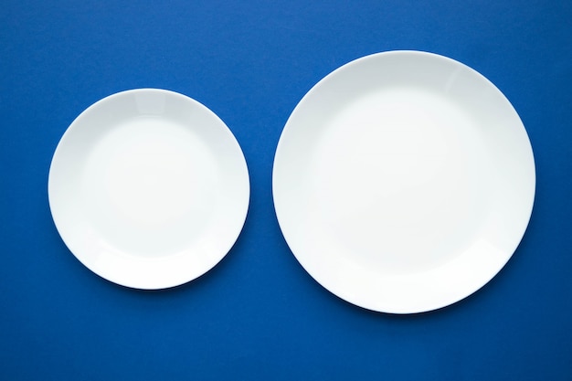 Dwa puste białe talerze na niebieskim stole, widok z góry