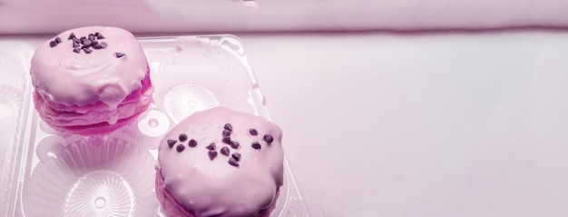 Dwa pyszne pączki z cukrem pudrem i kawałkami czekolady w przezroczystym plastikowym pojemniku baner z kopią miejsca po prawej różowy zabarwienie