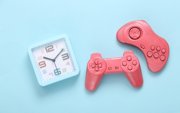 Dwa różowe gamepady z budzikiem na niebieskim tle Czas grać w gry wideo