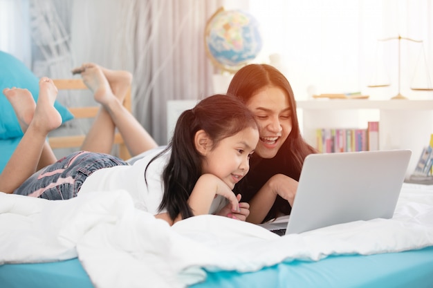 Dwa ślicznej Azjatykciej Dziecko Dziewczyny Używa Pastylkę I Laptop Na łóżku.