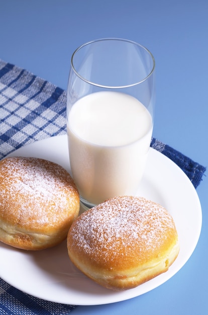 Dwa słodkie pączki i szklanka mleka na śniadanie na stole