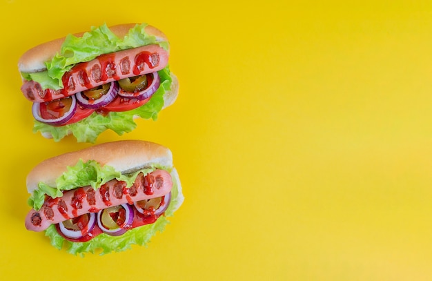 Dwa Soczyste Hot Dogi Z Grillowanej Kiełbasy Pomidorowej, Cebulowej Sałaty I Ketchupu Na żółtym Tle