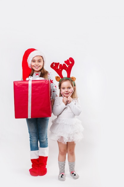 Dwa szczęśliwe małe uśmiechnięte dzieci w czapce Świętego Mikołaja i rogach jelenia z dużym świątecznym pudełkiem i słodyczami. czas świąt