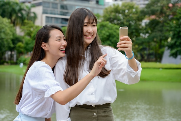 Dwa szczęśliwej młodej pięknej Azjatyckiej nastoletniej kobiety bierze selfie wpólnie przy parkiem