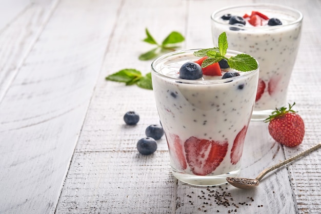 Dwa truskawkowe nasiona chia warstwowe smoothie lub koktajl mleczny z miętą truskawkową i jagodową w szkle na jasnoszarym tle. Letnie i zdrowe napoje dietetyczne, wegetariańska koncepcja żywności.