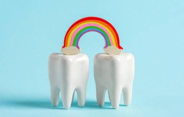 Zdjęcie dwa zęby z tęczą na niebieskim tle plakat reklamowy dla kliniki stomatologicznej w miesiącu dumy