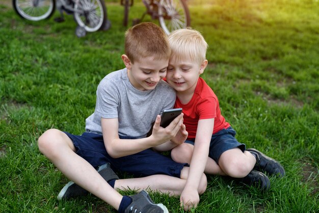 Dwaj chłopcy ze smartfonem w rękach siedzą na trawie.