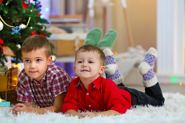 Dwaj śliczni Mali Bracia Leżą Na Dywanie Na Tle Choinki