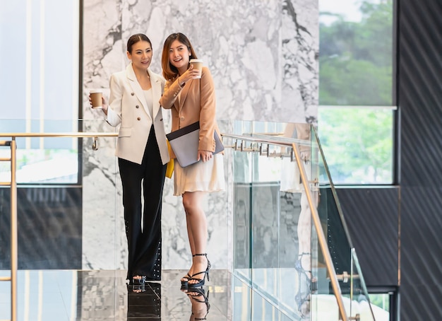 Dwie Azjatyckie Kobiety Biznesu Spacerujące I Rozmawiające Podczas Przerwy Na Kawę W Nowoczesnym Biurze Lub Przestrzeni Coworkingowej