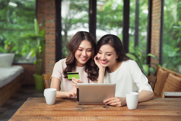 Dwie azjatyckie kobiety używają laptopa do robienia zakupów online z płatnością kartą kredytową