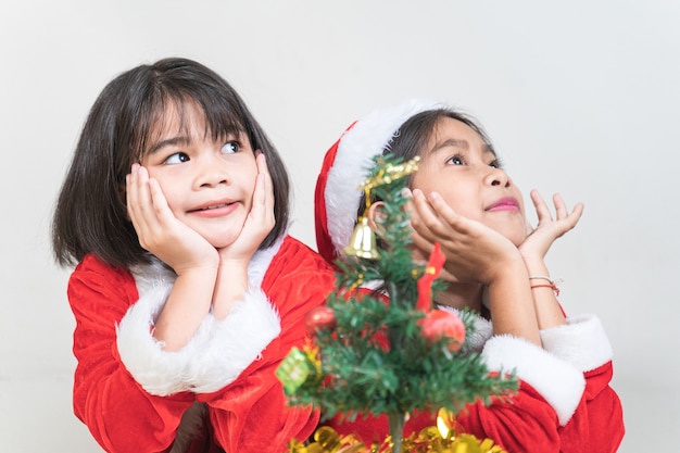 Dwie azjatyckie małe dzieci dziewczynki ubrane w czerwony strój Świętego Mikołaja, aby świętować Boże Narodzenie w domu