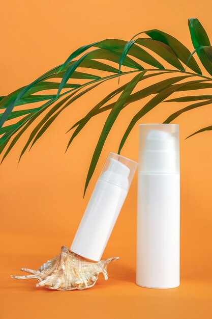 Dwie białe puste butelki po kosmetykach z filtrem przeciwsłonecznym, kremem do opalania lub innym produktem kosmetycznym, muszlą i palmą