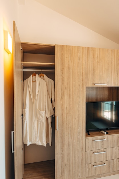 Dwie białe szaty w szafie z otwartymi drzwiami i wnęką pod telewizorem plazmowym