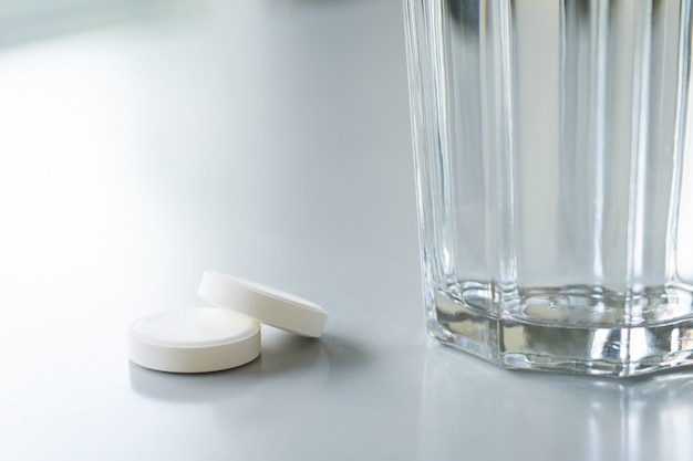 Dwie białe tabletki na stole w pobliżu szklanki z wodą. Chora osoba jest gotowa do przyjmowania tabletek