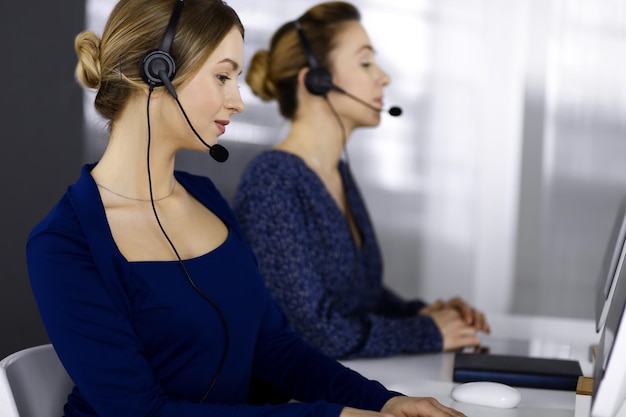 Dwie bizneswoman rozmawiają z klientami przez zestawy słuchawkowe, siedząc przy biurku w nowoczesnym biurze. Zróżnicowana grupa ludzi w call center. Telemarketing i obsługa klienta.