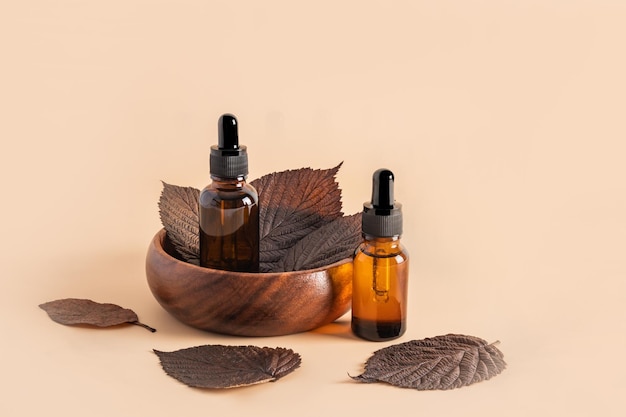 Dwie butelki kosmetyczne z pipetą na beżowym tle i brązowych jesiennych liściach naturalne kosmetyki do pielęgnacji skóry twarzy naturalna pielęgnacja