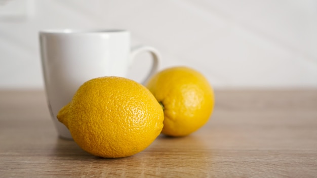 Dwie cytryny na kuchennym stole obok białego kubka herbaty. Koncepcja rano